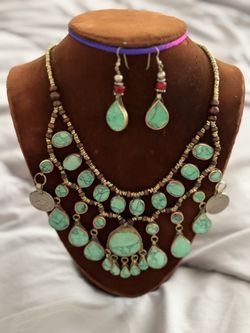 It features two cascading tiers of oval and teardrop turquoise stones. It is accented with small dark brown wooden spacer beads along the col