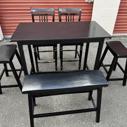 Black wooden table and two chairs and two stools and a bench