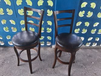 This is a set of two wooden bar stools featuring black faux leather seats.