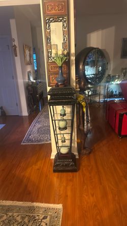 Beautiful tall decorative display stand with an elegant black finish, detailed design, sturdy metal sides and four glass shelves. This is a substantia