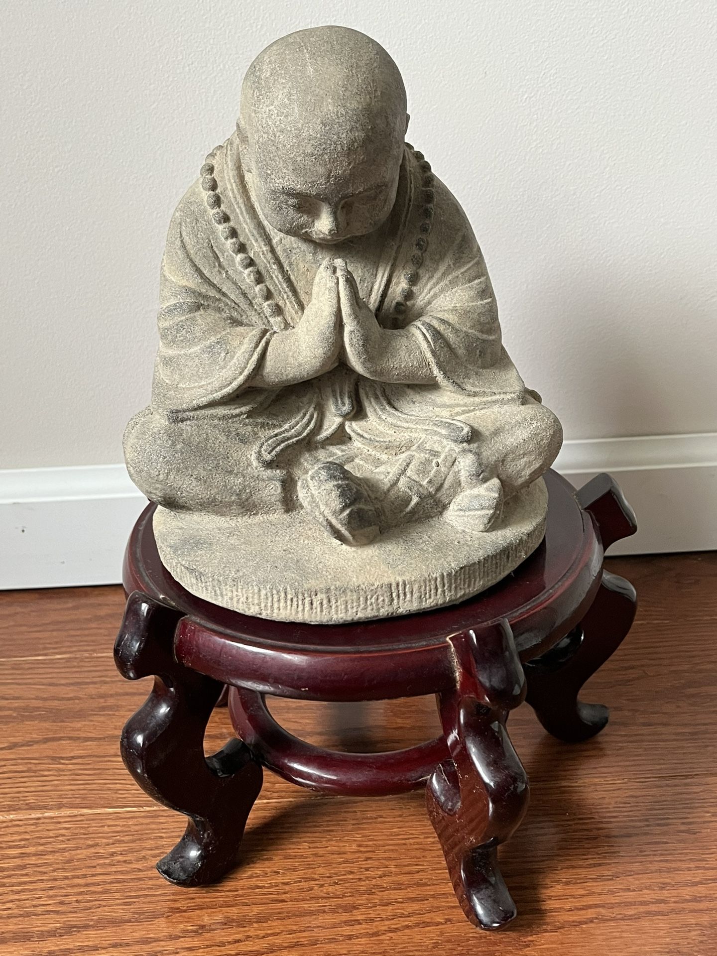 Volcanic Ash Nemaste Monk With Slightly Lowered Head On Top Of A Wooden Stand