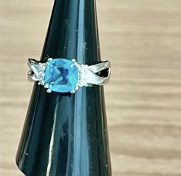 Elegant blue cushion-cut center stone set in a polished silver band. Stamped 925 Sparkling accent stones flank the center for added brilliance. Classi