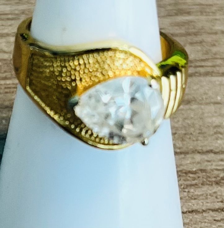 Elegant gold-tone women's ring featuring a sparkling clear solitaire stone. Polished gold finish complements the faceted clear centerpiece. Classic an