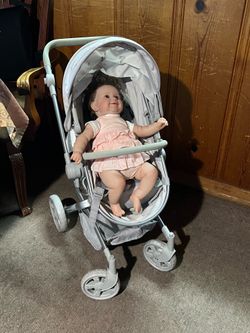 A toy stroller for dolls-specifically the convertible model from Pottery Barn Kids-with a baby doll included.color gray