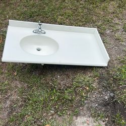 The image shows a white, single-basin bathroom sink with an integrated countertop and a single-handle faucet