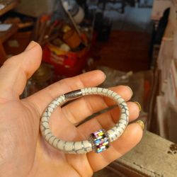 white or off-white python-embossed leather bracelet with a cylindrical magnetic clasp and a cube charm featuring multi-colored baguette-cut gemstones.