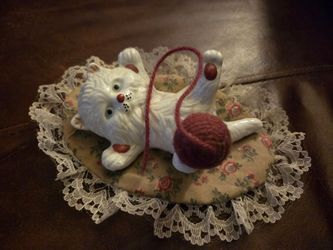 vintage ceramic cat figurine from the 1970s features a playful white cat lying on its back, adorned with a red yarn ball and resting on a delicate flo