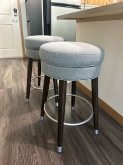 Grey swivel upholstered bar stools come in a set of two.