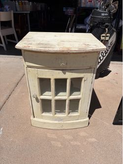 Charming small wooden cabinet has one door with glass panes and one pull out drawer. Distressed paint