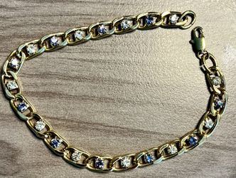 Elegant gold-tone chain bracelet featuring alternating blue and clear stones. Polished gold links add shine and a refined look. Suitable for everyday