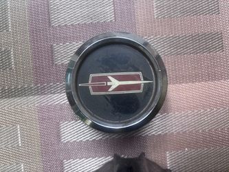 vintage Olds Cutlass Rally wheel center cap features a classic rocket/jet emblem set against a maroon and black center with a chrome outer ring
