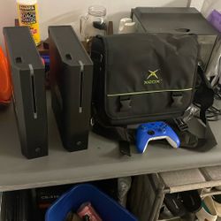 (2) Xbox (for parts) An Xbox Bag And One Controller