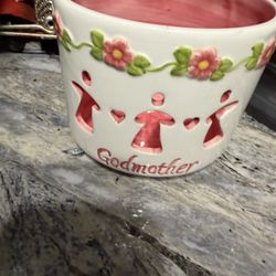 This ceramic tea light candle holder features cutouts of figures holding hands, hearts, and flowers with the word "Godmother" written on