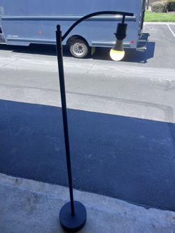 black arc floor lamp with a single, exposed LED bulb