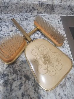 vintage vanity set featuring a hand mirror and matching brushes with textured brass-tone handles.