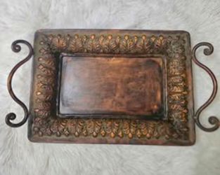 Decorative metal tray has an embossed leaf pattern border and ornate scroll handles. This rectangular piece is finished in a dark bronze or copper ton