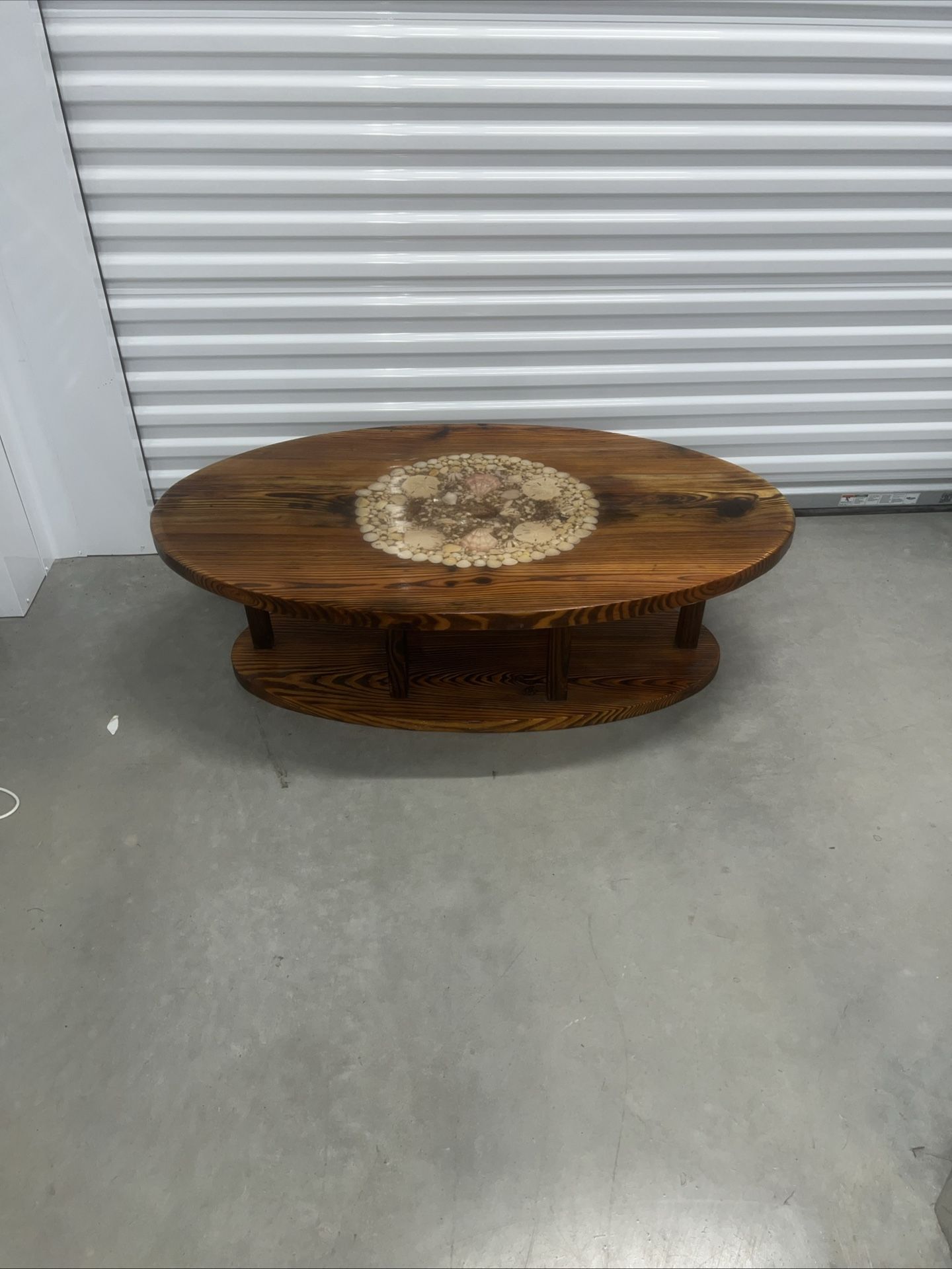 Coffee table with seashells in the middle. Used in good condition with some cosmetic blemishes. The table has a hard plastic coating that covers the e