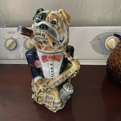 a collectible bulldog figurine, specifically a beer stein, featuring a bulldog dressed in a tuxedo and holding a saxophone while smoking a cigar