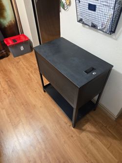 Black metal file cabinet with a flip-top lid and front door, loaded with green hanging file folders. Features a mesh side panel, open bottom shelf.