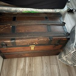 This item is an antique wooden steamer trunk with dark metal hardware and a flat top.