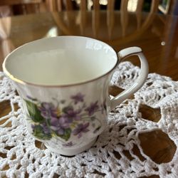 China coffee cup featuring a beautiful white design with gold trim and vibrant purple flowers.