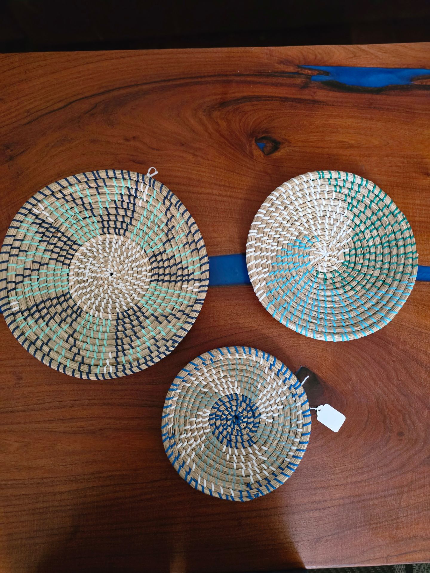 Set of three handwoven straw wall baskets in natural tones with blue and green accent patterns. Lightweight and decorative, they add texture and a coa
