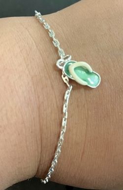 Delicate silver bracelet featuring a playful green and cream flip-flop charm. Lightweight, everyday piece that adds a touch of summer to any outfit. T