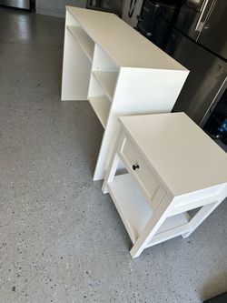 A white desk/workstation with open shelving &  white nightstand with one drawer and a lower shelf.