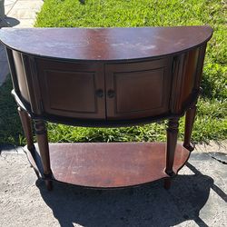 This traditional-style console table, characterized by its half-moon (or demilune) shape and dark wood finish, is a versatile piece ideal for entryway