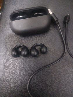pair of black open-ear clip-on wireless Bluetooth earbuds with a matching charging case and a USB-C charging cable.