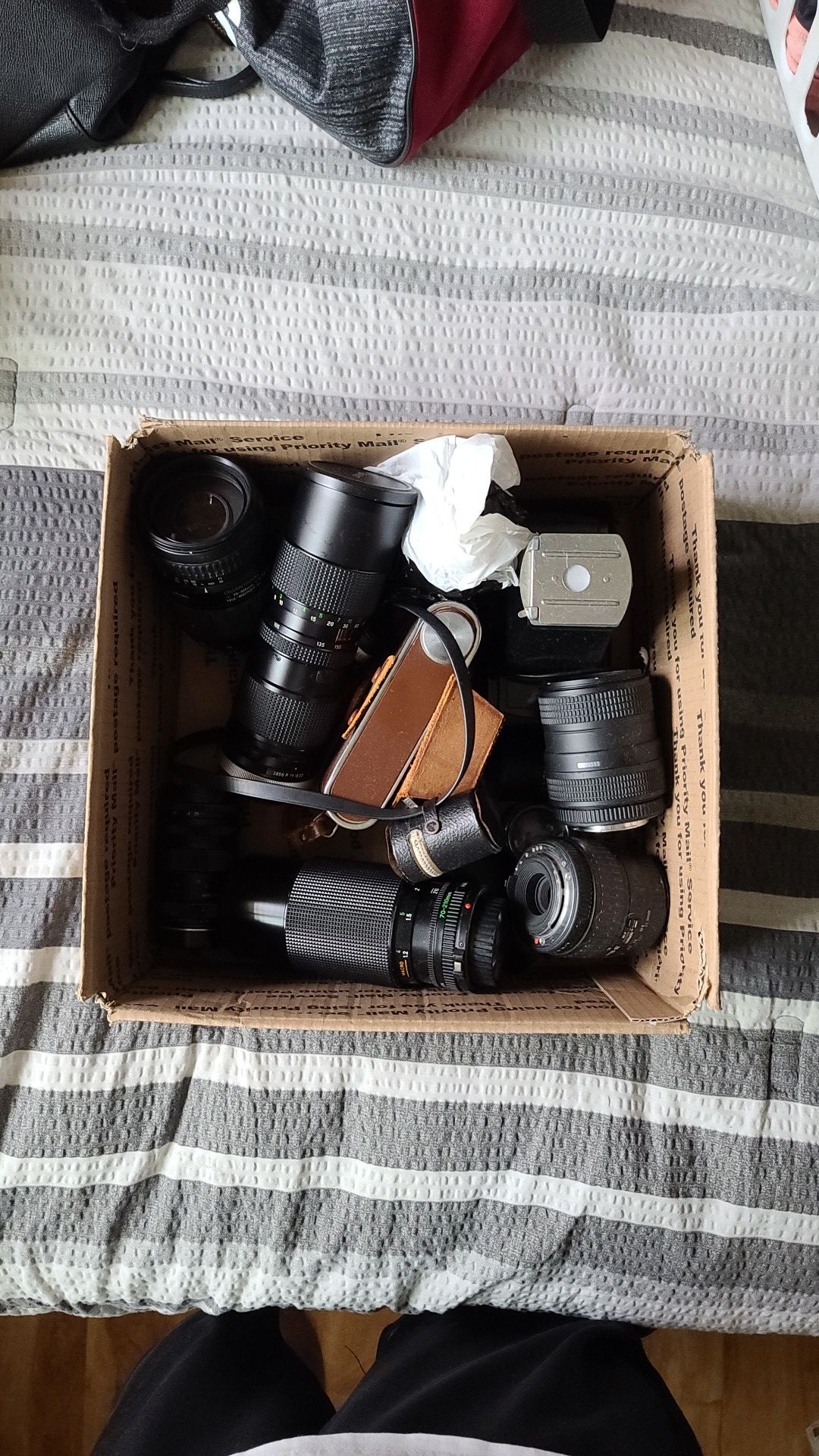 Box full of random SLR camera lenses. Included is a Ricoh 35 with leather case