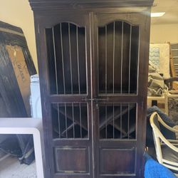 Vintage dark wood wine cabinet featuring metal bar enclosures on the upper doors and built-in wine racking