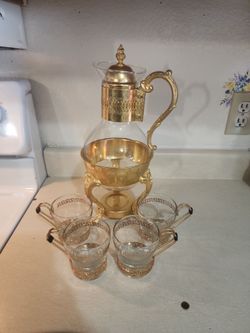 This vintage-style glass &gold metal tea set typically features a carafe with a warming stand designed for a candle.