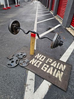 100 Pounds total. Black EZ curl bar loaded with cast iron weight plates on both ends. Plates show surface rust and wear from regular use. Bar is in fu