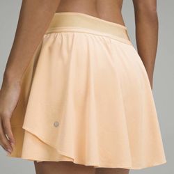 Lululemon Court Rival High-Rise Skirt in the "Summer Glow" orange color, featuring a distinctive ple