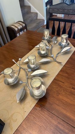 decorative silver-toned metal centerpiece appears to be the Crate & Barrel Carissa Pillar Candelabra, featuring a branched vine design accented with t