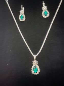 Elegant faux Emerald jewelry set with a silver-tone finish. This set has a necklace with a teardrop-shaped Emerald stone pendant surrounded by clear c