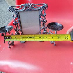 This product is a vintage silver-tone metal picture frame featuring an ornate, scrollwork border and attached candle holders. 