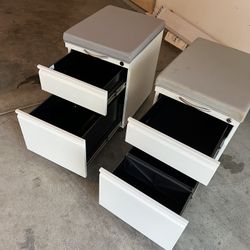 Set Of 2 White Metal Filing Cabinets With Gray Cushions On Top With Wheels