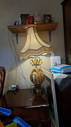 vintage-style table lamp features a distinctive amber glass body and a ornate, fringed fabric shade.
