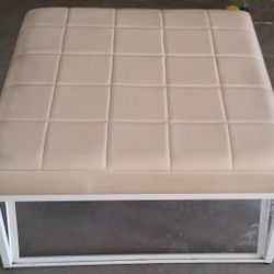 This is a modern beige faux leather ottoman or bench with a white metal frame