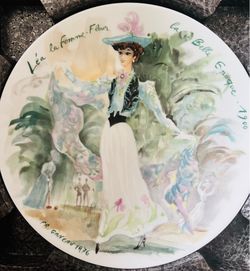 This plate is a 1976 D'Arceau Limoges "Léa la Femme-Fleur" from the "Les Femmes Du Siecle" series, featuring delicate watercolor-style artwork of a wo