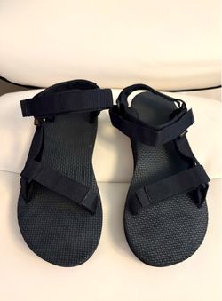 The sandals are the Teva Original Universal model in black, characterized by their quick-drying adjustable straps and a durable rubber sole.