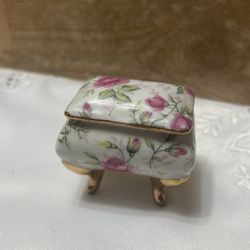 vintage, hand-painted porcelain trinket box with a pink rose pattern and gilded feet.
