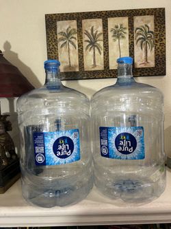 Two recently emptied 5 gallon water bottles with handles and caps as shown