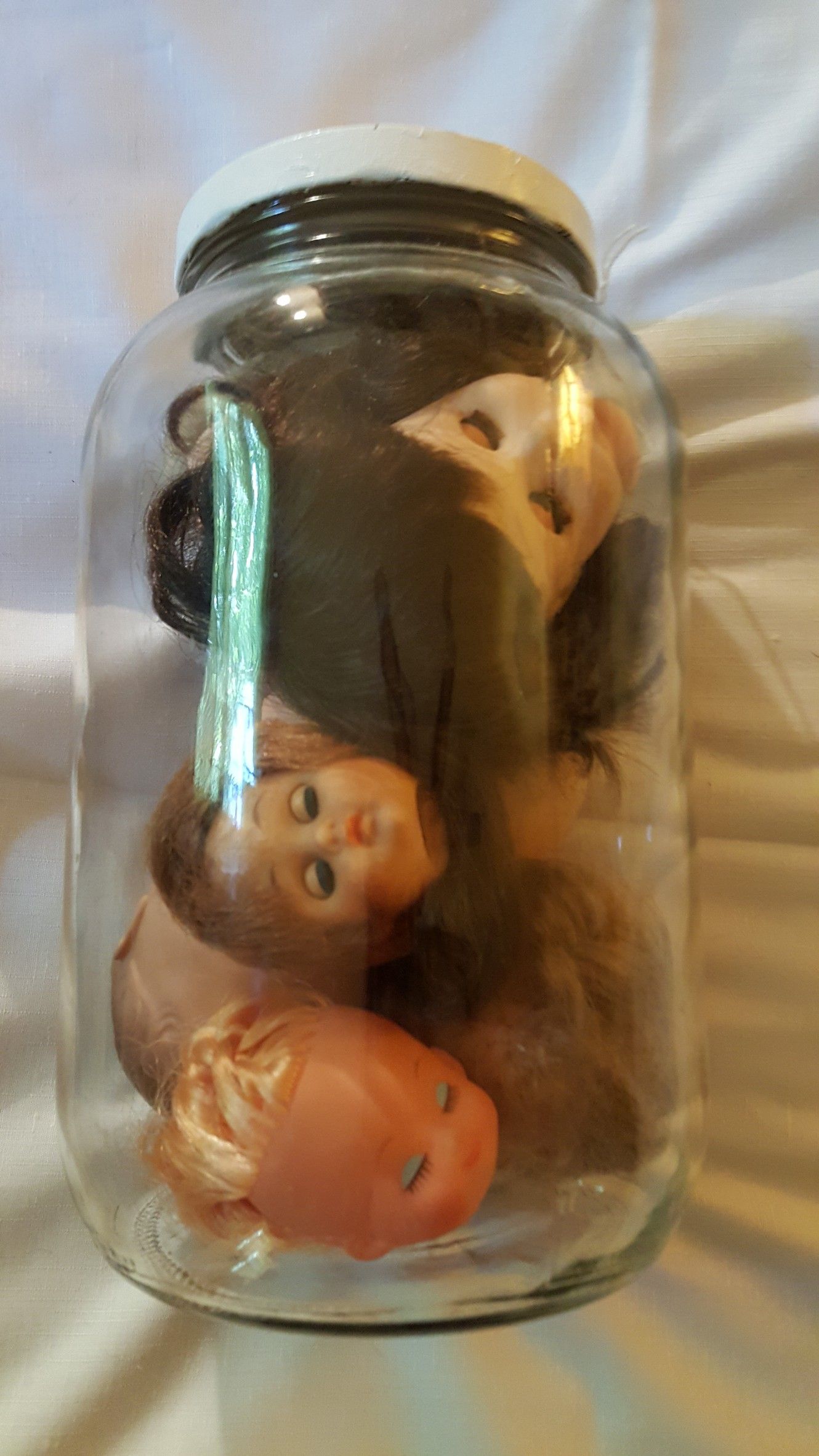 Vintage doll heads in a glass jar