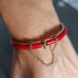 Red hinged clamper bracelet with safety chain still intact. Metal red cuff bracelet.