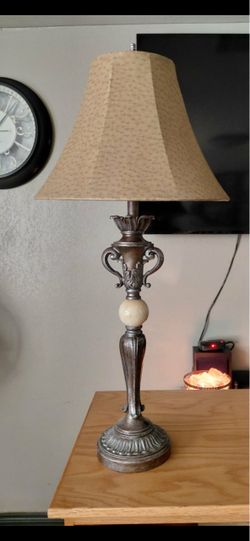 This Kathy Ireland Amor Collection table lamp features a distressed bronze finish and a distinctive beige bell shade.