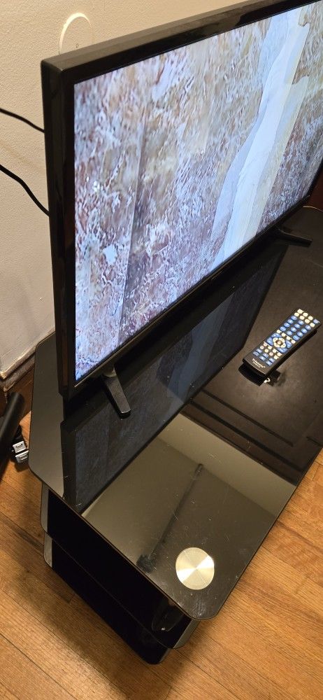 Entertainment center made of glass and metal includes TV. The TV has a 28" screen.