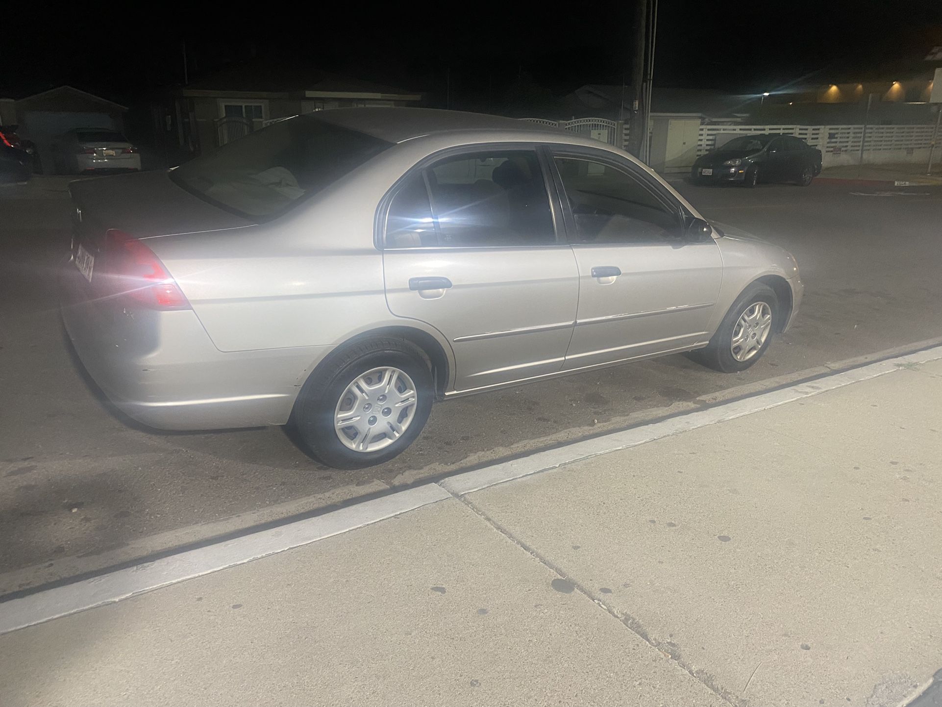  A silver Honda Civic, a fuel-efficient and economical car, is parked on a suburban street at night.